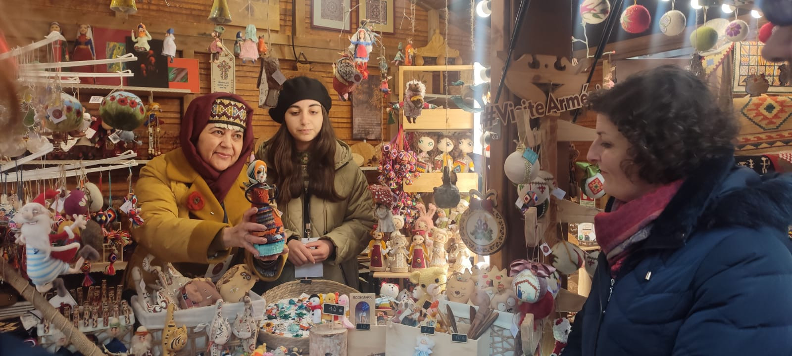 © Cassandre Thomas. Allah montre les créations à la mairesse de Strasbourg, Jeanne Barseghian. Meri se charge de la traduction. Un chalet arménien au marché de Noël de Strasbourg
